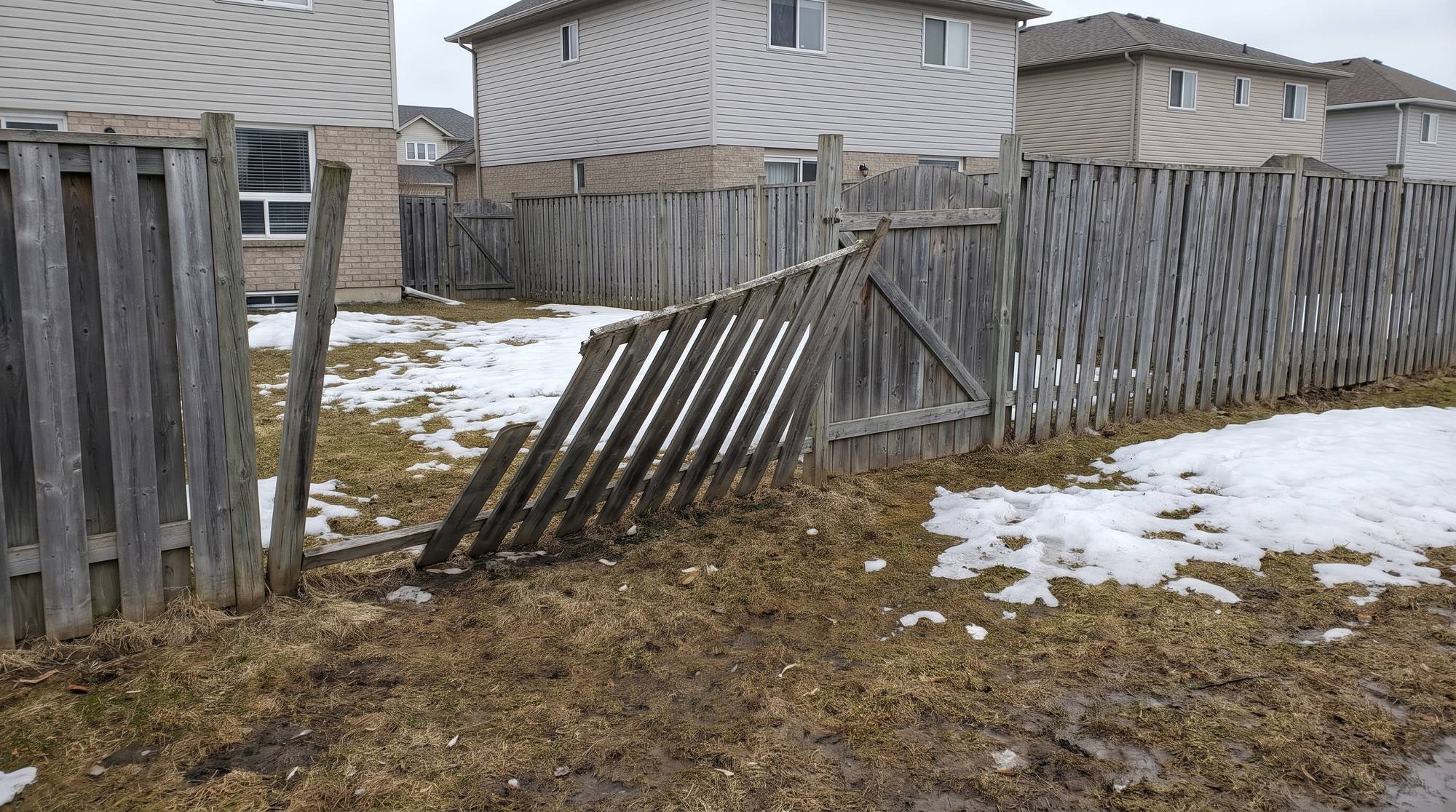 An old wood fence with leaning, frost-heaved posts and a collapsed section in early spring