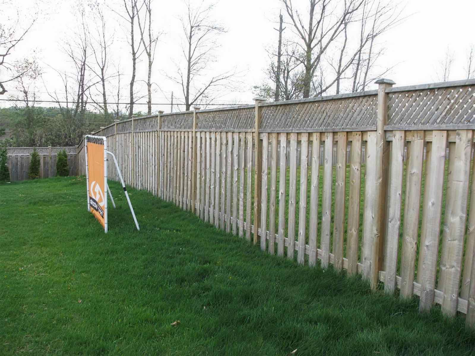 A long run of lattice-capped wood fencing across a wide green lawn