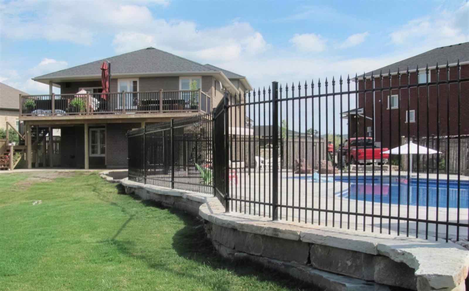 Black iron pool fence with spear-top pickets curving along a stone retaining wall beside an in-ground pool